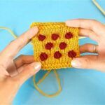 two hands are holding a piece of yarn with red flowers on it and the other hand is knitting