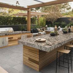 an outdoor kitchen with granite counter tops and bar stools next to the bbq