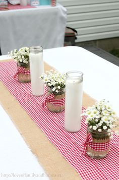 three mason jars filled with baby's breath daisies on a red and white checkered table runner