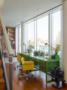 an office with green desk and yellow chairs in front of large windows overlooking the city