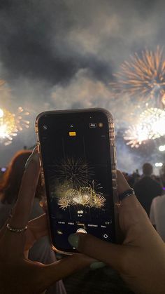 someone holding up their cell phone to take a photo with fireworks in the background