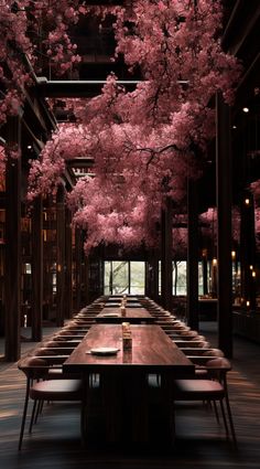 a long table with chairs under pink trees in the middle of an indoor dining area