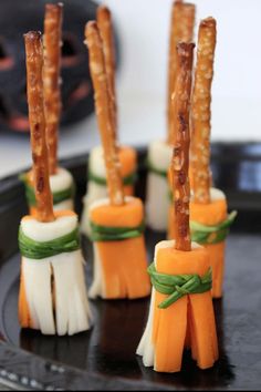 small carrot sticks with cheese and green ribbon on them sitting on a black plate in front of a white wall