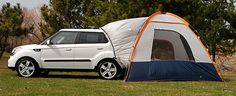 a white car parked next to a tent in the grass