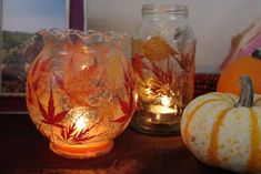 three glass vases sitting on top of a table next to pumpkins and candles