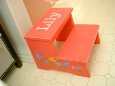 an orange wooden step stool with flowers painted on the bottom and letters that spell it out