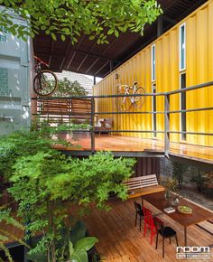 an outdoor deck with tables and chairs next to a yellow shipping container that's attached to the side of a building