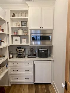 a kitchen with white cupboards and shelves filled with coffee machines, toasters, and other appliances