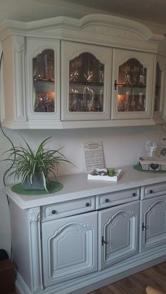 a white china cabinet with glass doors and plants on top