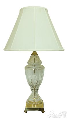 a clear glass lamp with a white shade on the base and a gold metal base