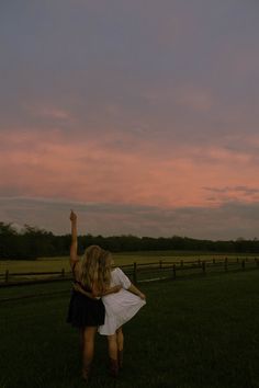 two people standing in the grass flying a kite at sunset or dawn with pink clouds behind them