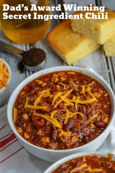 two bowls filled with chili and cheese next to bread on a wooden table, text reads dad's award winning secret ingredient chili