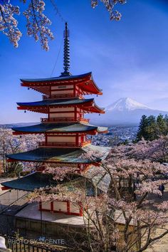 the pagoda is surrounded by cherry blossom trees and mountains in the distance, with snow - capped mountain in the background