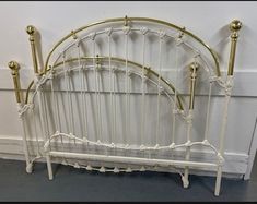 a white iron bed frame with gold colored posts and headboard, against a wall