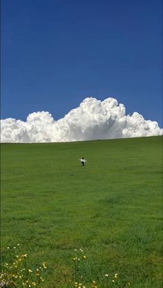 two people in a large field flying kites under a cloudy blue sky with fluffy white clouds