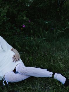 a woman sitting in the grass with her legs crossed wearing white stockings and tights