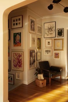 a living room filled with lots of framed pictures on the wall above a black chair