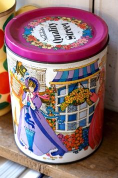 a colorful tin with an image of a woman on it next to a cup and saucer