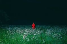 a man in a red suit standing in tall grass at night with the light on