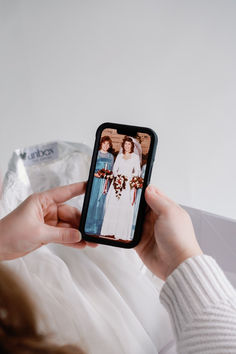 a woman holding up a cell phone with an image of two women in white dresses