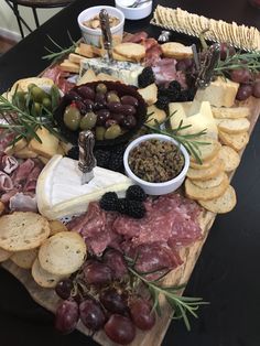 an assortment of cheeses and meats on a wooden platter with olives