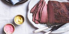 a white plate topped with sliced meat next to two bowls of dips and sauce