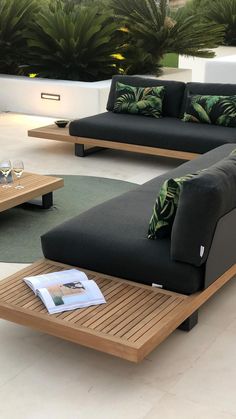 an outdoor living room with black couches and green pillows on the floor, surrounded by palm trees