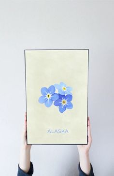 a person holding up a poster with blue flowers on it that says alaska in the center