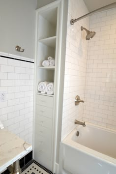 a white bathroom with black and white tile flooring on the shower wall, tub and sink