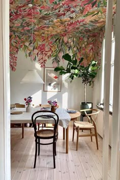 an open door leading to a dining room with floral wallpaper on the ceiling and wooden chairs