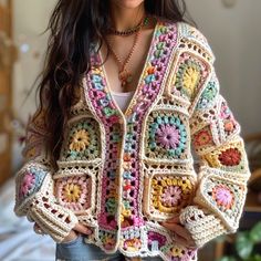 a woman wearing a colorful crochet jacket standing in front of a bed with her hands on her hips