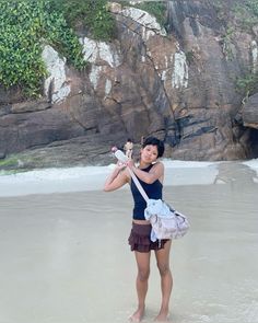 a woman standing on the beach holding a flower in one hand and an umbrella in the other