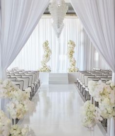 the aisle is lined with white flowers and draping for an elegant wedding ceremony