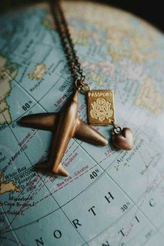 an airplane charm hangs from a globe on a gold plated necklace with a heart