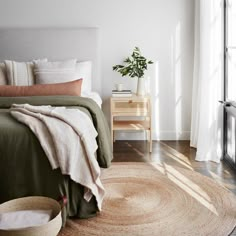 a bedroom with a bed, rug and window in the corner that has white curtains