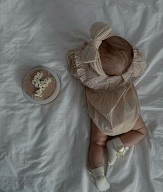 a baby laying on top of a white bed next to a plate with food in it