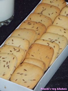 a white box filled with cookies next to a glass of milk on a black table