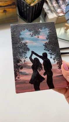 a person holding up a painting with the image of two people dancing in front of them