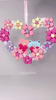 a heart shaped ornament with stars hanging from it's sides and two bears in the middle