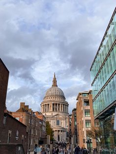 people walking down the street in front of some buildings and a dome building with a clock on it