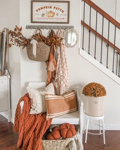 a white bench topped with lots of pillows and pumpkins next to a stair case