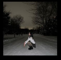 a woman kneeling down in the snow with her hand on her hip and looking up into the sky