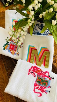 three embroidered napkins sitting on top of a wooden table next to a vase with flowers