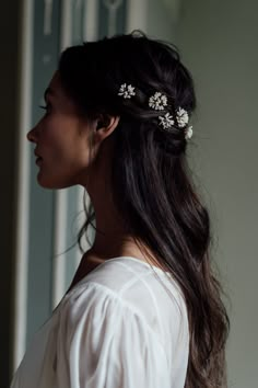 a woman with long dark hair wearing a white blouse and flowers in her hair is looking off into the distance