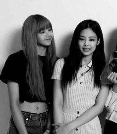 three young women standing next to each other in front of a wall holding cell phones