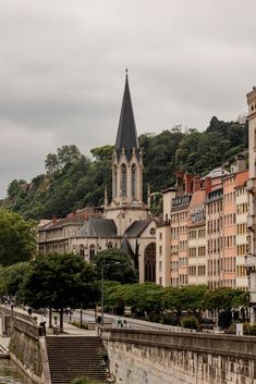 an old church on top of a hill next to a river and buildings in the background