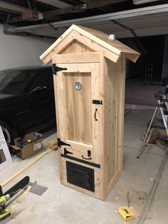 a small wooden outhouse sitting in a garage next to a black car and tools