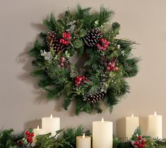 a christmas wreath with pine cones, holly and berries is hung on the wall next to candles