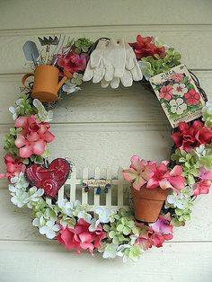 a wreath is hanging on the side of a house with flowers and gardening utensils