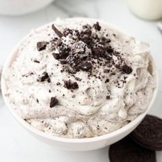 a close up of a bowl of food on a table with cookies and milk in the background